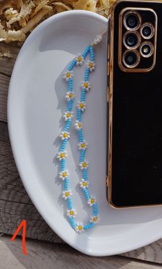 a white plate topped with a blue and yellow beaded necklace next to an iphone