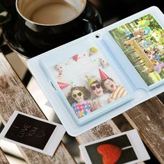 an open photo album sitting on top of a wooden table next to a cup of coffee