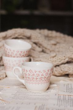 two coffee cups sitting on top of a table next to an open book and blanket