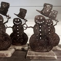 three metal snowmen with hats and tails on top of each other, sitting on wood planks