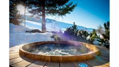 a hot tub sitting on top of a wooden deck next to snow covered ground and trees