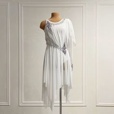 a white dress on a mannequin stand in front of a wall