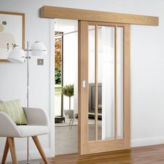 an open door in a living room next to a white chair and wooden flooring