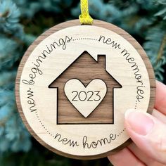 someone holding up a wooden ornament with a house in the shape of a heart