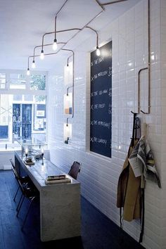 a long table in a room with white tile walls and wooden floors, along with hanging lights