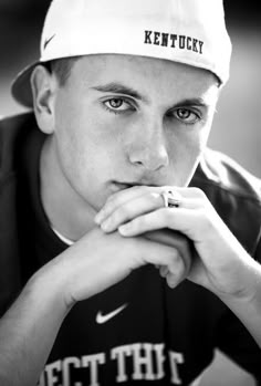 a black and white photo of a young man wearing a hat with his hands on his chin