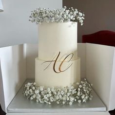 a three tiered white wedding cake with flowers on the side and monogramming