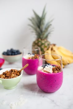 three bowls filled with granola, yogurt and blueberries next to bananas