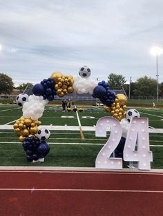 a large balloon arch decorated with soccer balls and streamers at the end of a football field