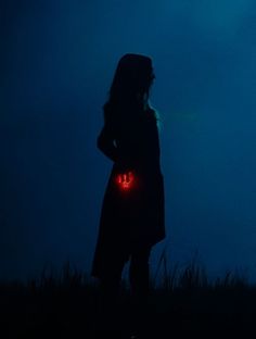 a woman standing in the dark with her back turned to the camera, holding an illuminated heart