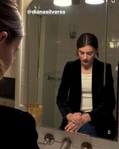 a woman standing in front of a bathroom mirror looking at her hands on the sink