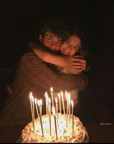 two people hugging each other in front of a cake with candles