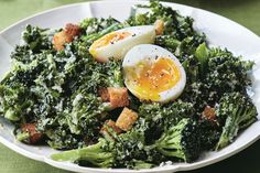 a white plate topped with broccoli covered in an egg and croutons