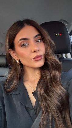 a woman sitting in the back seat of a car with long hair and earrings on