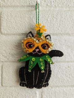 a black cat ornament hanging on a brick wall with beads and sequins