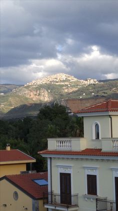 a view of some buildings and mountains in the distance with dark clouds above them on a cloudy day