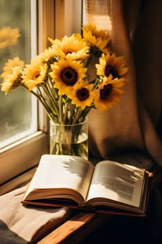 an open book sitting on top of a wooden table next to a vase filled with sunflowers