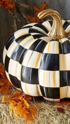 a black and white checkered pumpkin sitting on top of dry grass next to autumn leaves