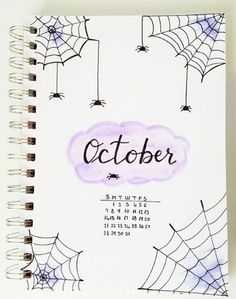 a spiral notebook with the word october written on it and spider webs hanging from strings