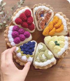 a person is holding a crocheted plate with different foods on it, including bread and berries