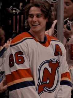 a young man in an orange and white jersey is smiling at the camera while people are taking pictures behind him