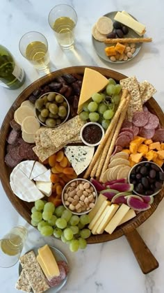 a wooden platter filled with cheese, crackers and grapes