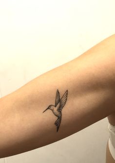 a small tattoo on the arm of a woman with a hummingbird flying above it