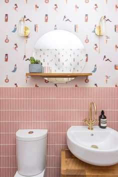 a bathroom with pink and white wallpaper has a mirror above the sink, along with a gold faucet