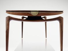 a wooden table with an oval shaped top and two curved legs on one end, in front of a white background