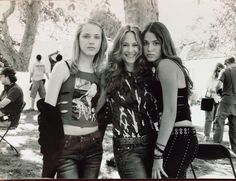 three young women standing next to each other in front of a group of people on the grass