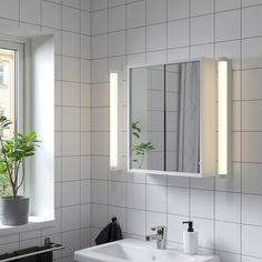 a bathroom with a sink, mirror and plant in the window sill next to it