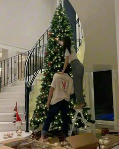 two people standing on ladders in front of a christmas tree