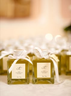 four square bottles with labels on them are sitting on a white tablecloth, tied with a white ribbon