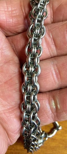 a hand holding a silver chain on top of a wooden table