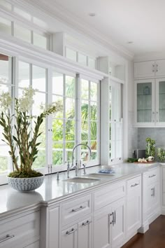 a large kitchen with white cabinets and wooden flooring, along with a bowl of flowers on the counter