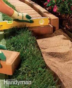 someone is using gardening tools to trim the grass in their garden area with bricks and pavers