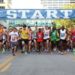 a large group of people running down a street in front of a sign that says start