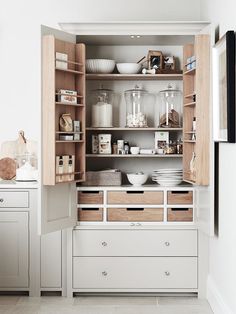 an open cabinet in a kitchen filled with white dishes and other items on top of wooden shelves