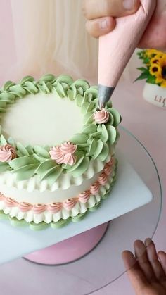 a person is cutting into a cake with a pink and green frosting decoration on it