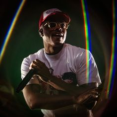 a man with glasses and a red hat on holding a microphone in front of colored lights