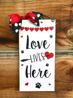 a sign that says love lives here with hearts and paw prints on it, hanging on a wooden wall