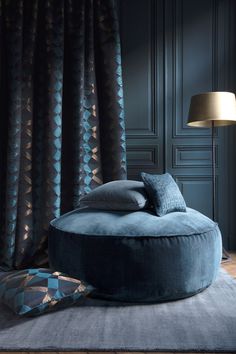 a large blue round ottoman sitting on top of a rug next to a lamp and pillows