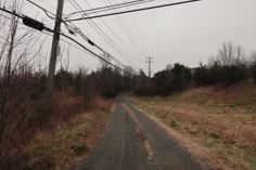 an empty dirt road with power lines and telephone poles in the distance on a gloomy day