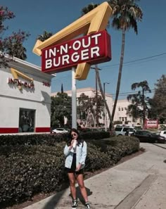 a woman standing in front of a sign for a fast food restaurant that says in - n - out burger