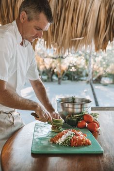 a man cutting up vegetables on top of a wooden table next to a pot and pan