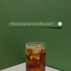 a glass filled with ice sitting on top of a table next to a sign that says where can i get the best coffee in town?