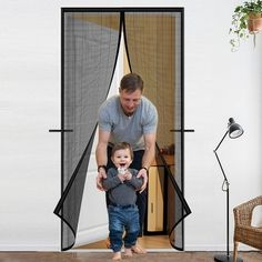 a man holding a toddler in front of a screen door with the child standing inside