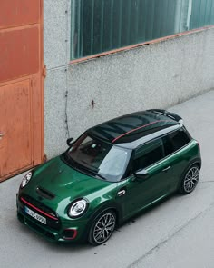 a green mini cooper parked on the side of a road next to a building and door