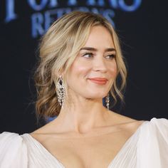 a woman in a white dress posing for the camera with her hair pulled back and wearing large earrings