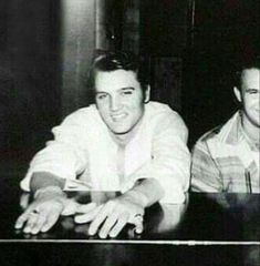 two men sitting next to each other in front of a table with a keyboard on it